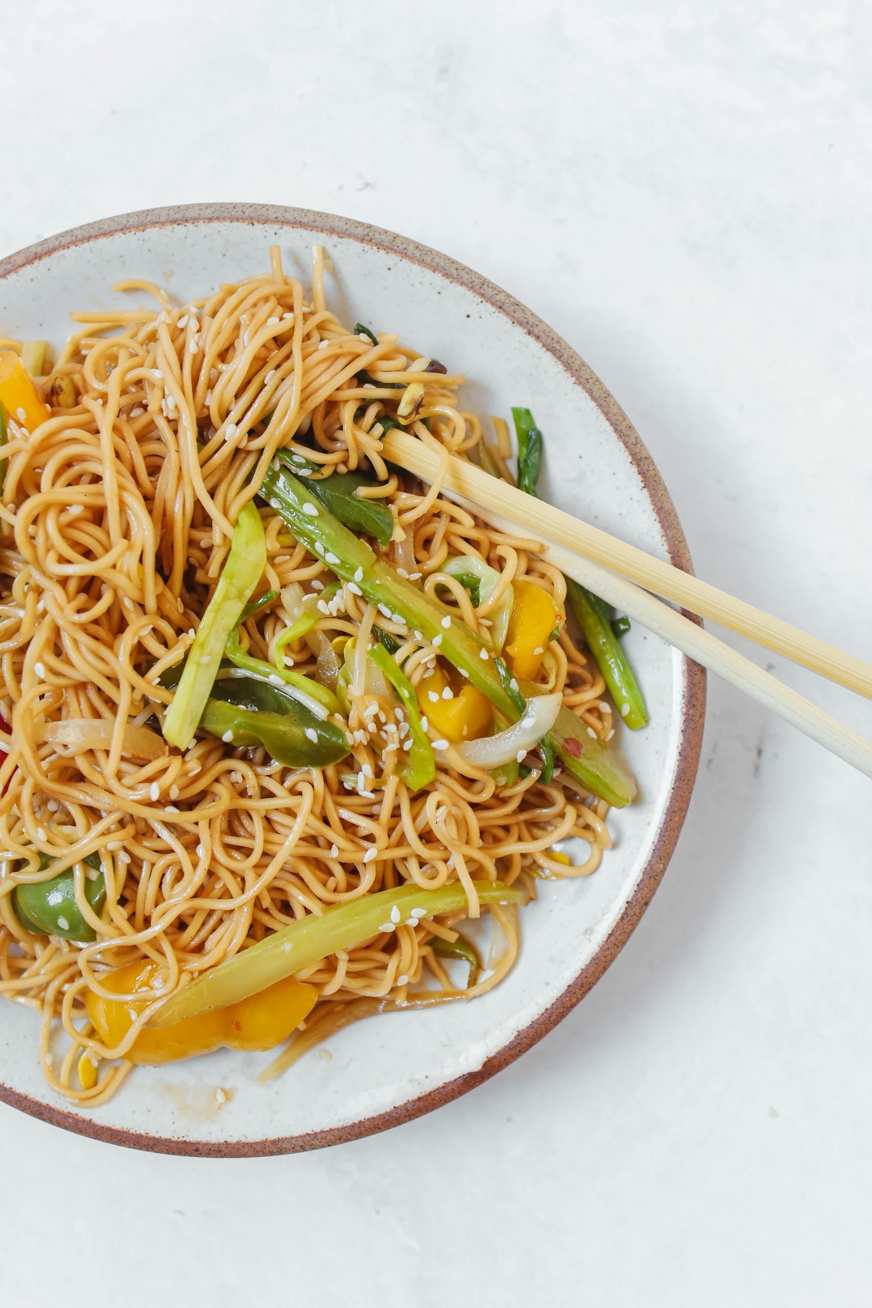 A dish of Asian noodles topped with colorful vegetables, served with chopsticks.