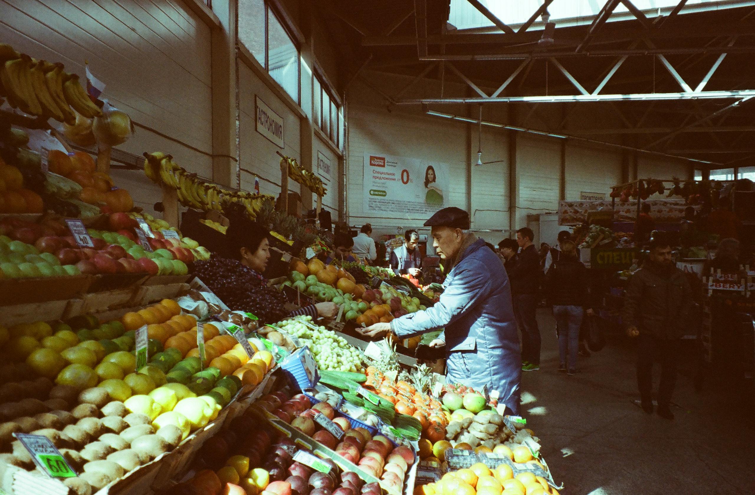 A bustling indoor market with vibrant fresh fruits and vegetables on display and people shopping.